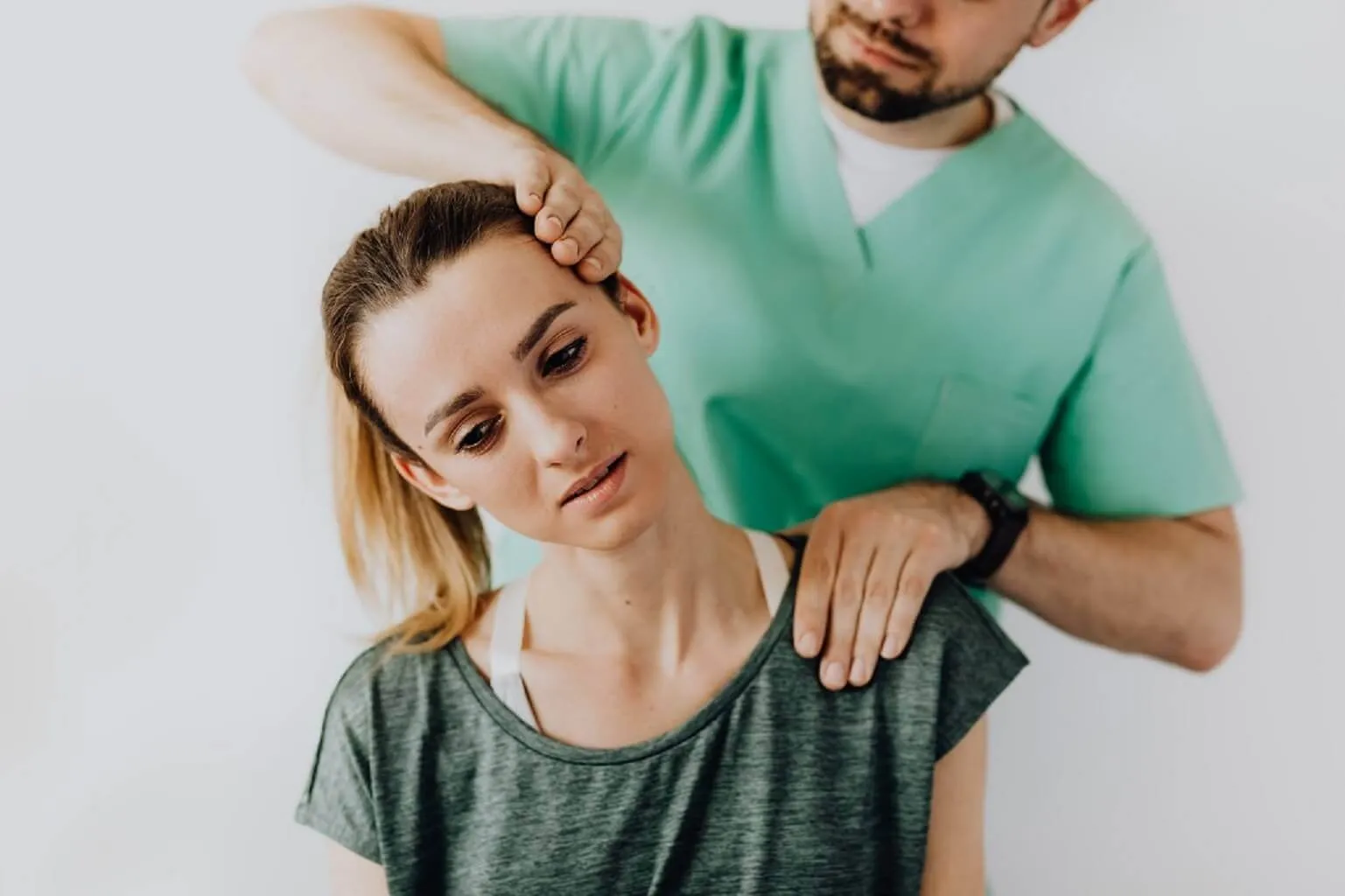 穿綠色刷手服的治療師站在後方，一手扶住女性頭部側邊、一手壓住肩膀，帶她把頸部往側邊傾斜